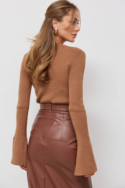Woman wearing a brown ribbed sweater and leather skirt against a white background