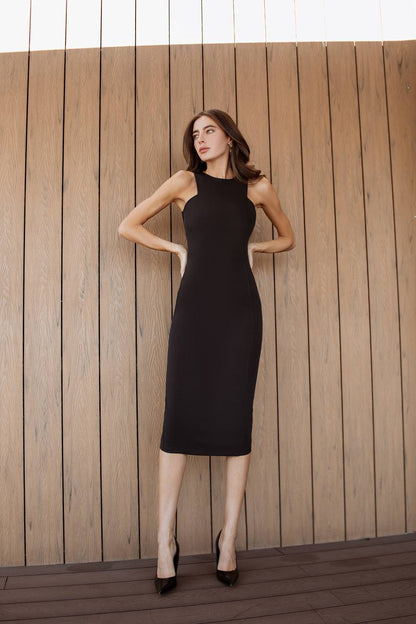 Woman in a black dress standing against a wooden wall