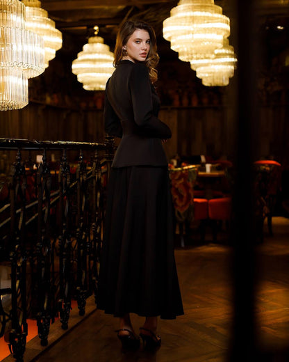 Woman in a black outfit standing in a dimly lit room with chandelier lights.
