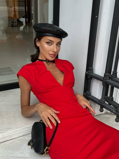 Woman in a red dress and black beret holding a black handbag indoors.