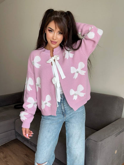 Woman wearing a pink sweater with white bow patterns and light blue jeans indoors.
