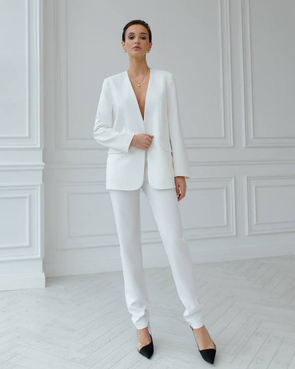 Woman wearing a white suit standing in a minimalistic room with white walls and floor.