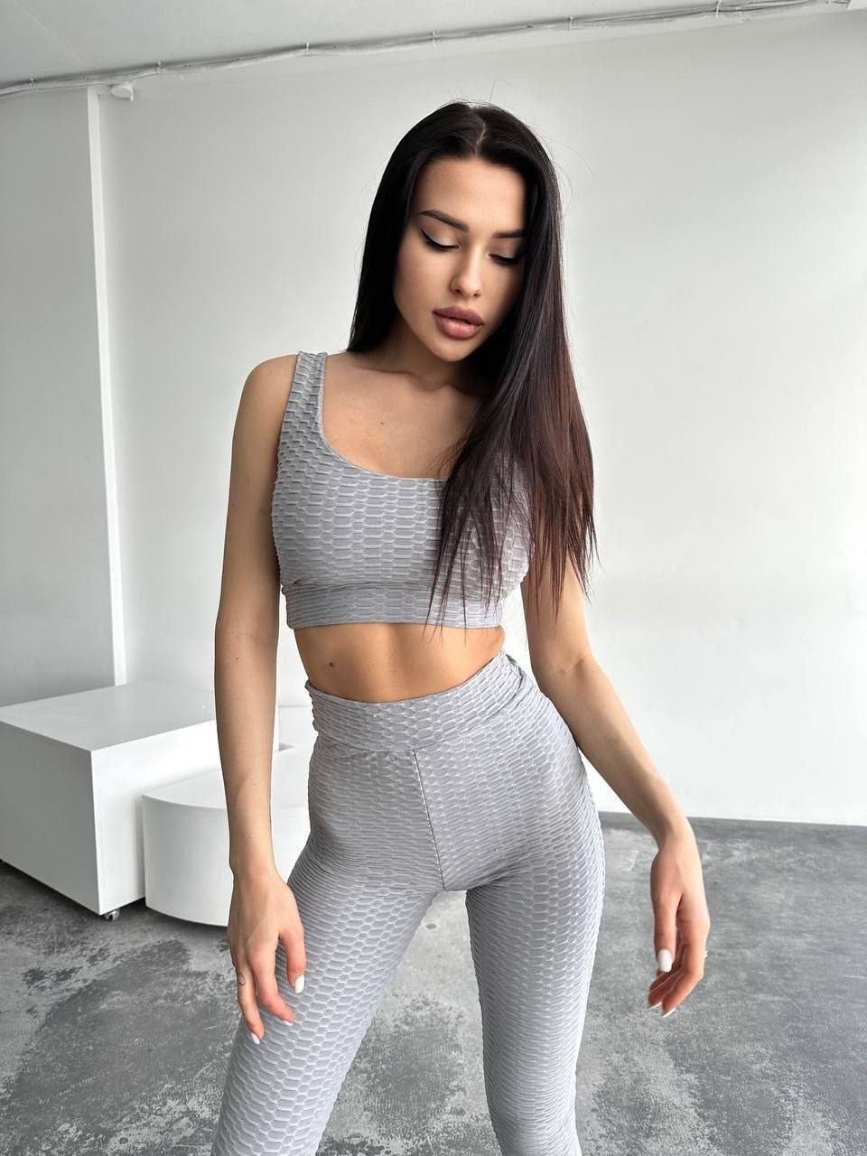Woman wearing a gray athletic outfit in a minimalistic setting