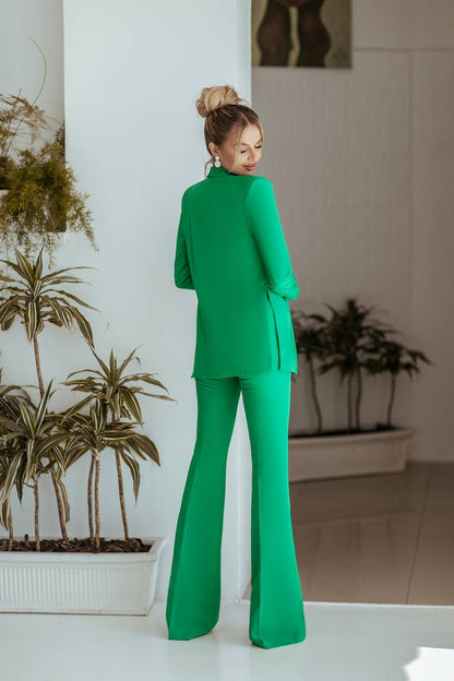 Woman in a green suit standing in a room with plants.