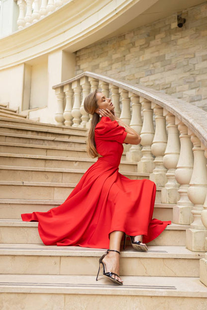 Woman in a red dress sitting on stone steps with a stone wall background