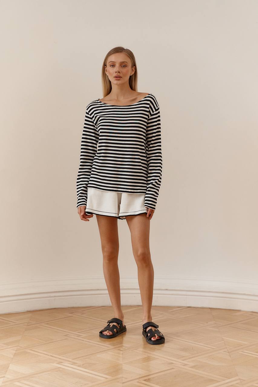 Woman wearing a black and white striped sweater and white shorts standing on a wooden floor.
