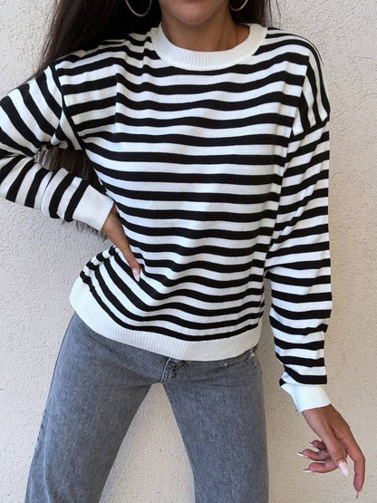 Person wearing a black and white striped sweater with gray jeans against a beige wall.