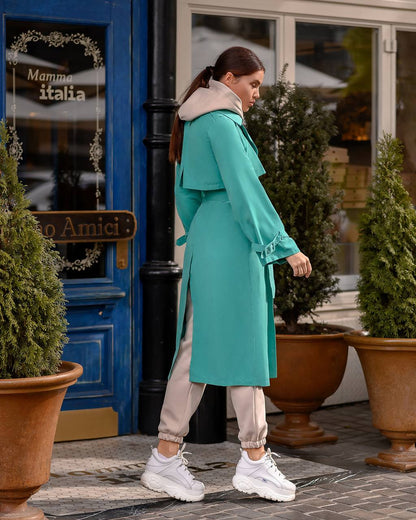 Woman in a teal coat standing outside a building with potted plants.