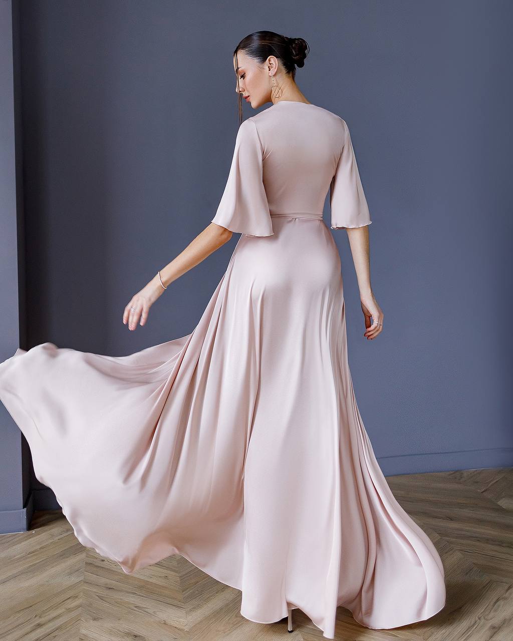 Woman in a flowing pink dress against a plain background