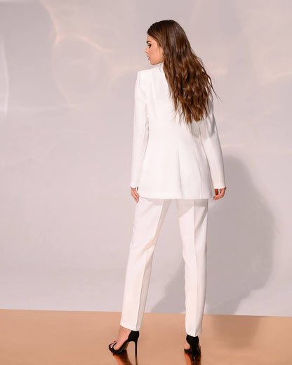 Woman wearing a white suit standing against a plain background