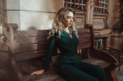 Woman in a green dress sitting on a wooden bench outdoors.