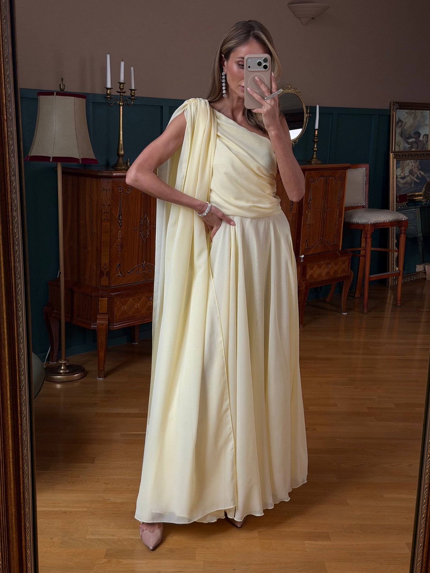Woman in a white saree taking a mirror selfie in a room with wooden furniture and decor.