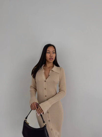 Woman wearing a beige ribbed dress holding a black handbag against a plain background