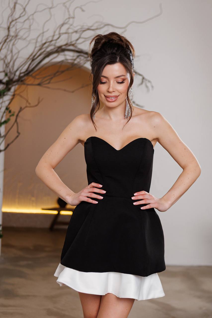 Woman wearing a black strapless dress with a white hem in an indoor setting.