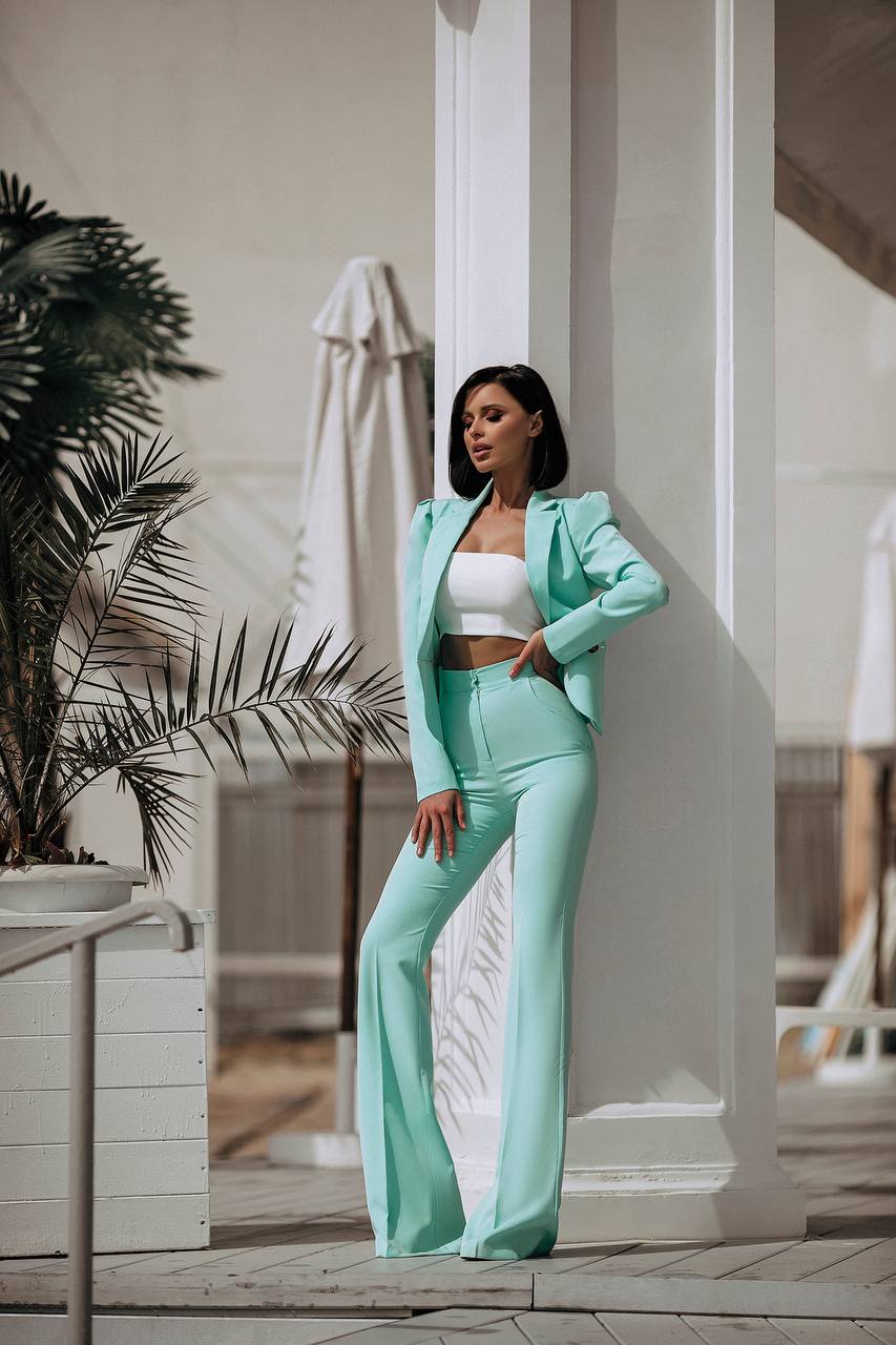 Woman in a mint green outfit standing in an outdoor setting with plants and columns.