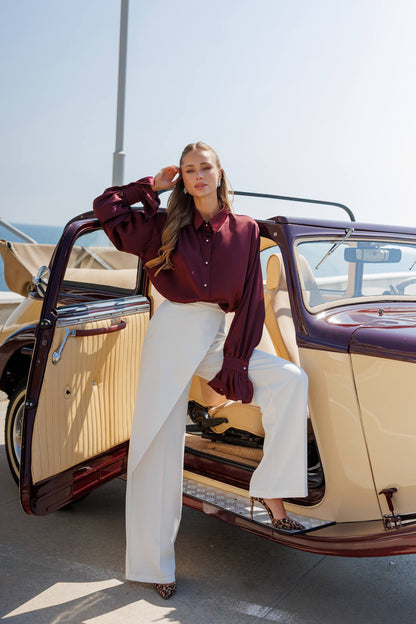 Woman in a red blouse and white pants sitting in an open car door.