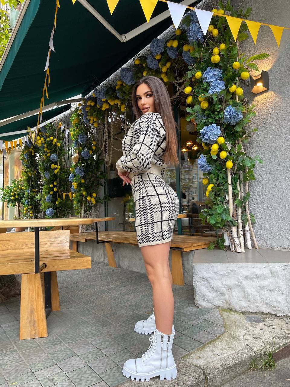 Woman in a stylish outfit standing in front of a decorated outdoor cafe.