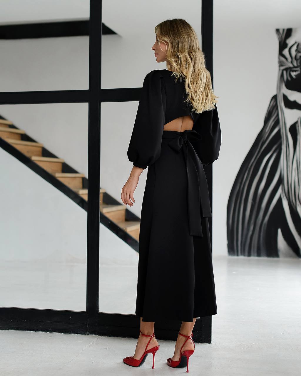 Woman wearing a black dress with cut-out design in a modern interior setting.