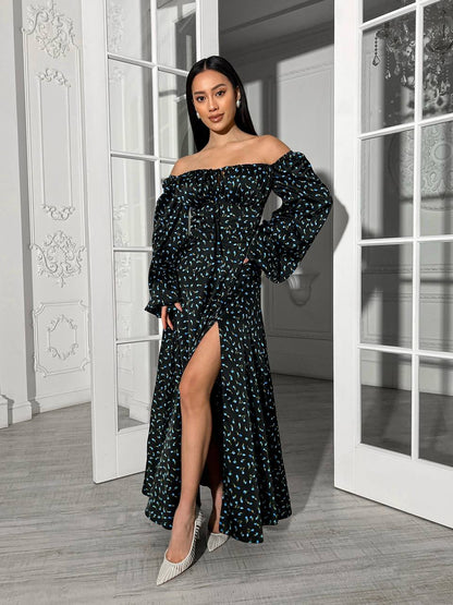 Woman in a black floral off-shoulder dress standing in a room with white walls and wooden floor.