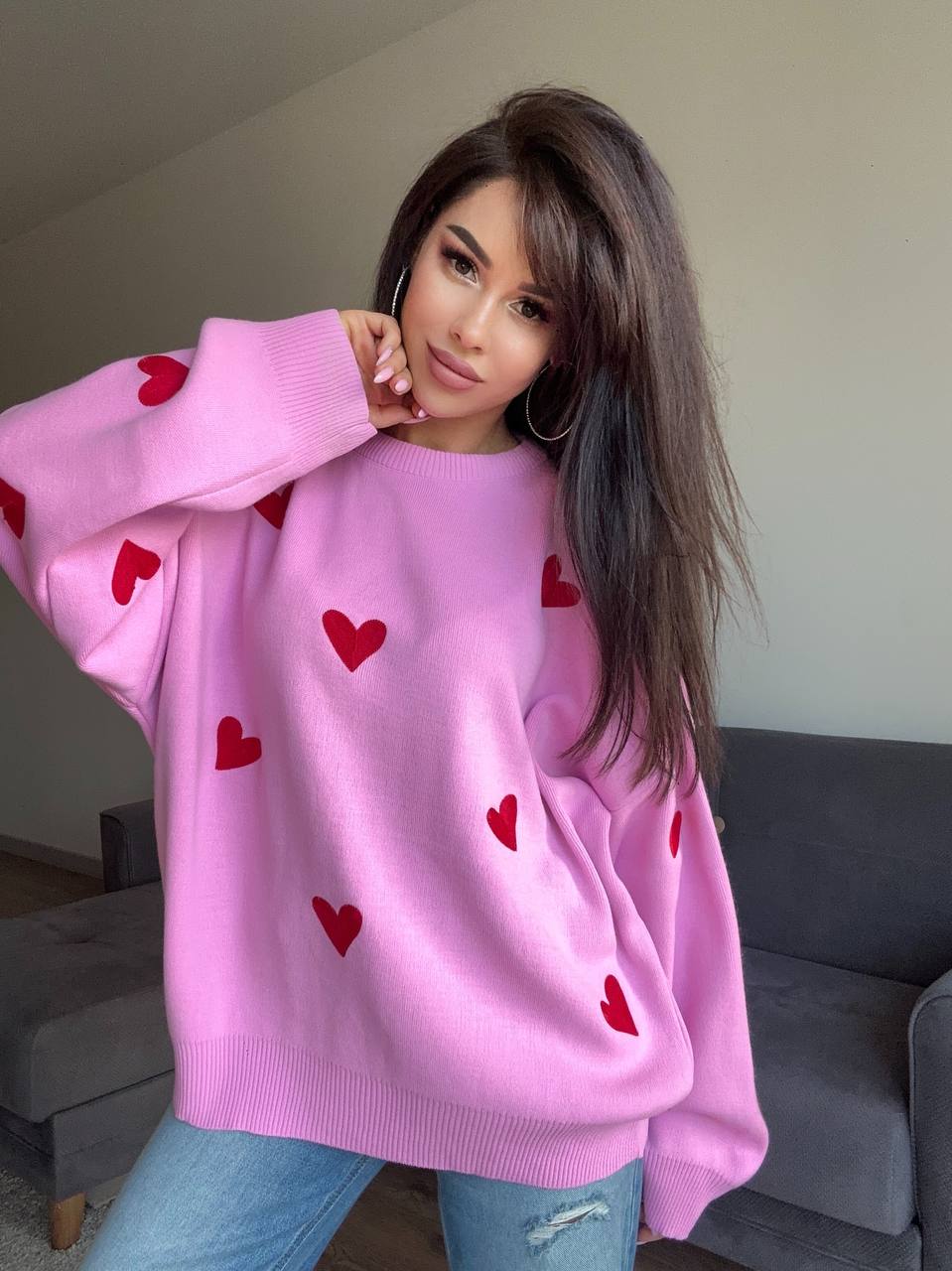 Woman wearing a pink sweater with red heart patterns indoors.