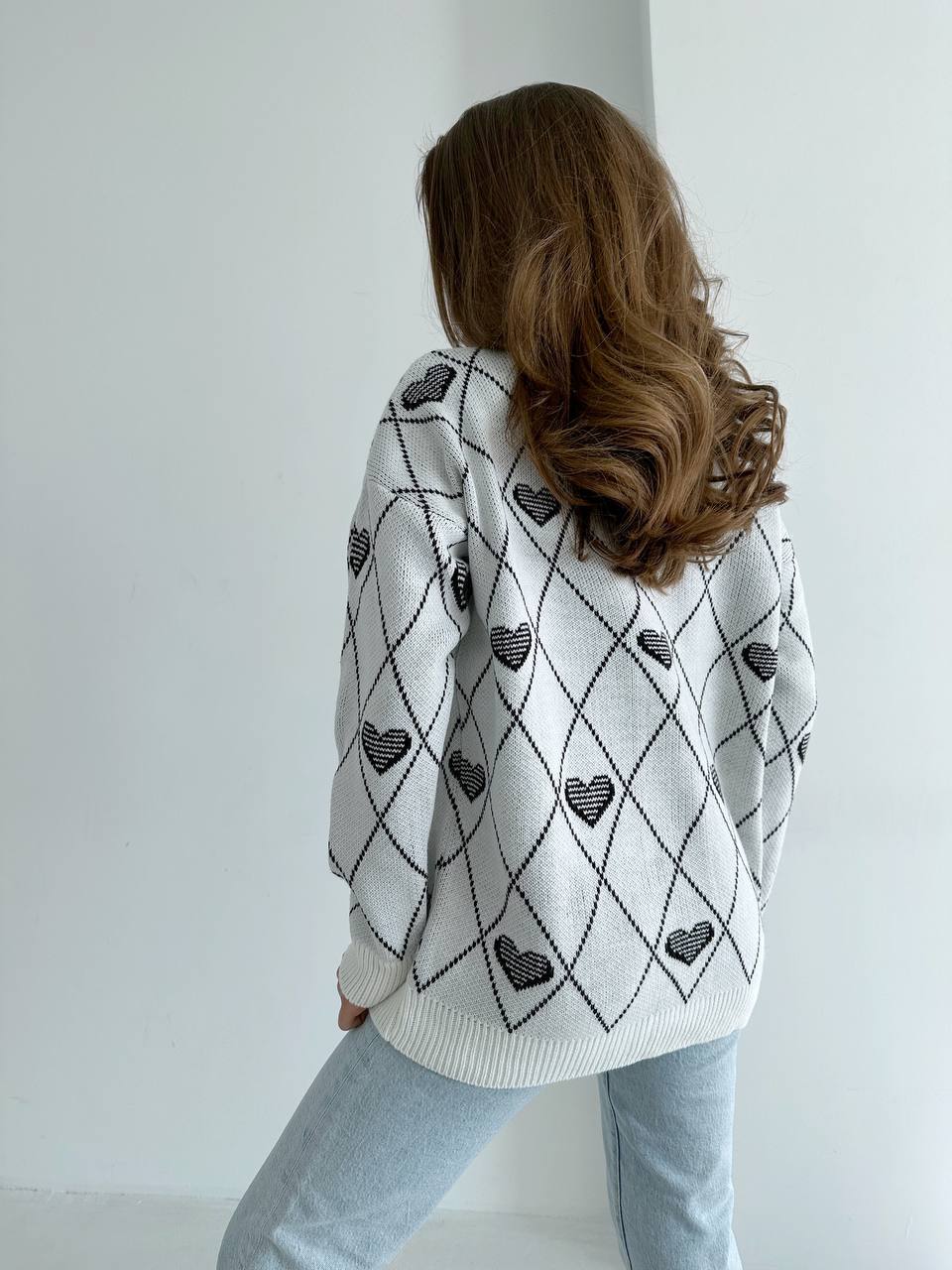 Person wearing a white sweater with black heart patterns against a plain background