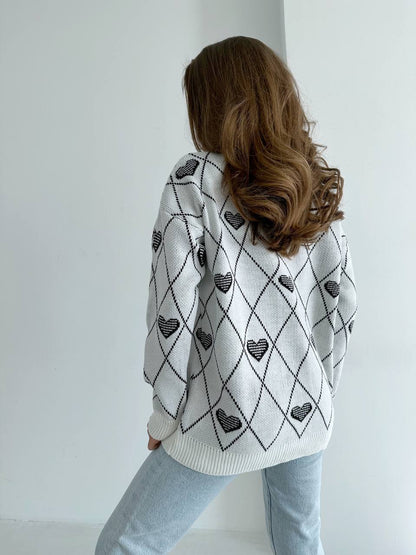 Person wearing a white sweater with black heart patterns against a plain background