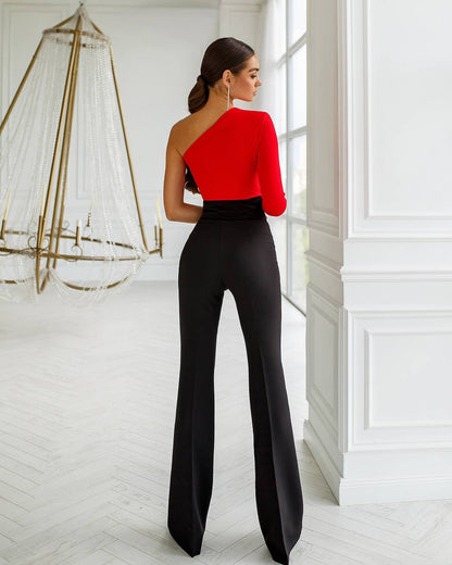 Woman wearing a red one-shoulder top and black pants in a stylish interior setting.