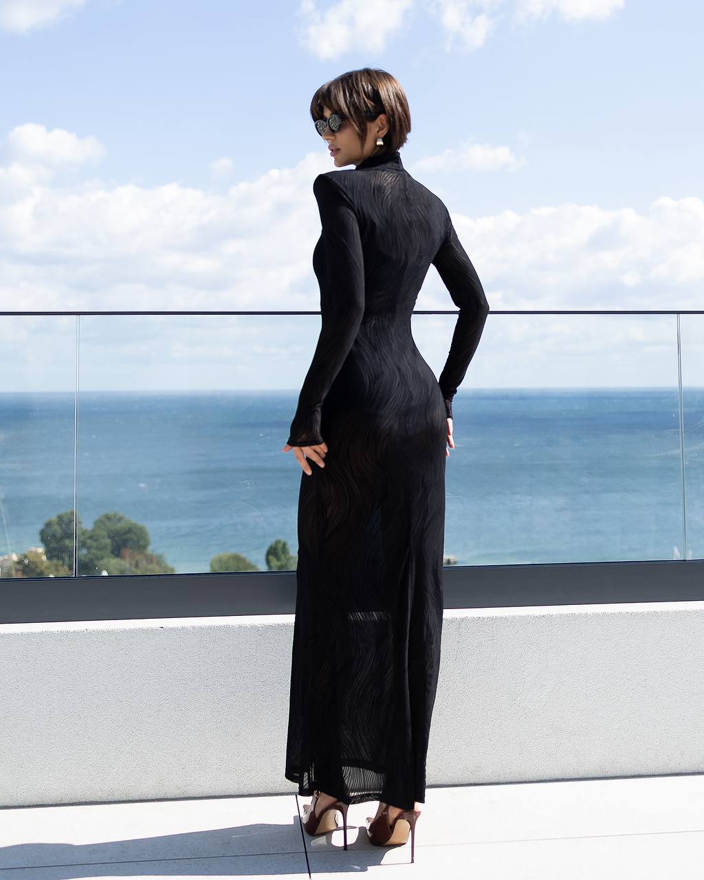 Woman in a black dress standing on a balcony with ocean view
