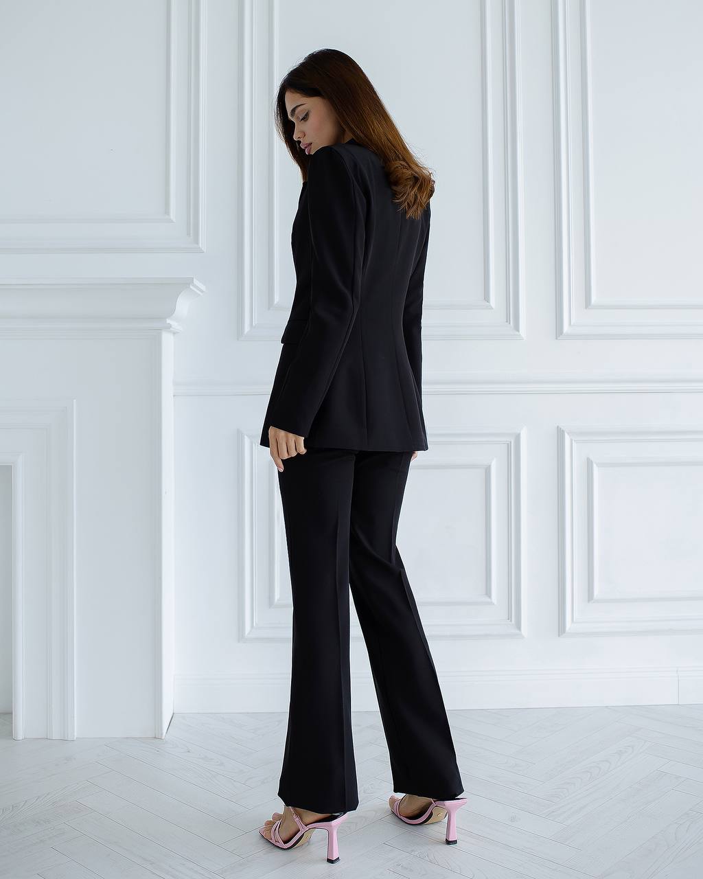 Woman wearing a black suit standing against a white paneled wall.