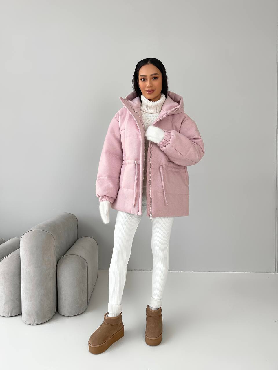 Person wearing a pink puffer jacket with a white background