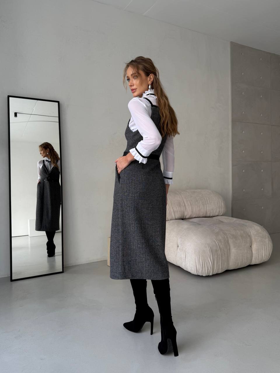 Woman in a gray dress standing in a minimalistic room with a large mirror.