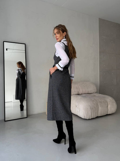 Woman in a gray dress standing in a minimalistic room with a large mirror.