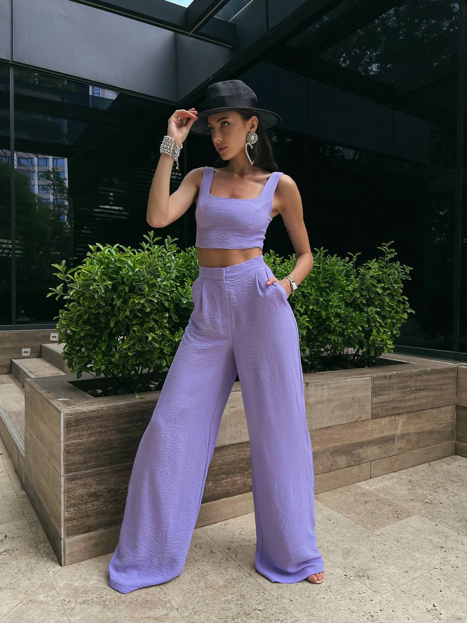 Woman in a lavender outfit posing outdoors with greenery in the background