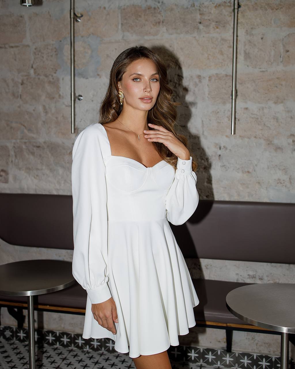 Woman wearing a white dress in an indoor setting with a stone wall background