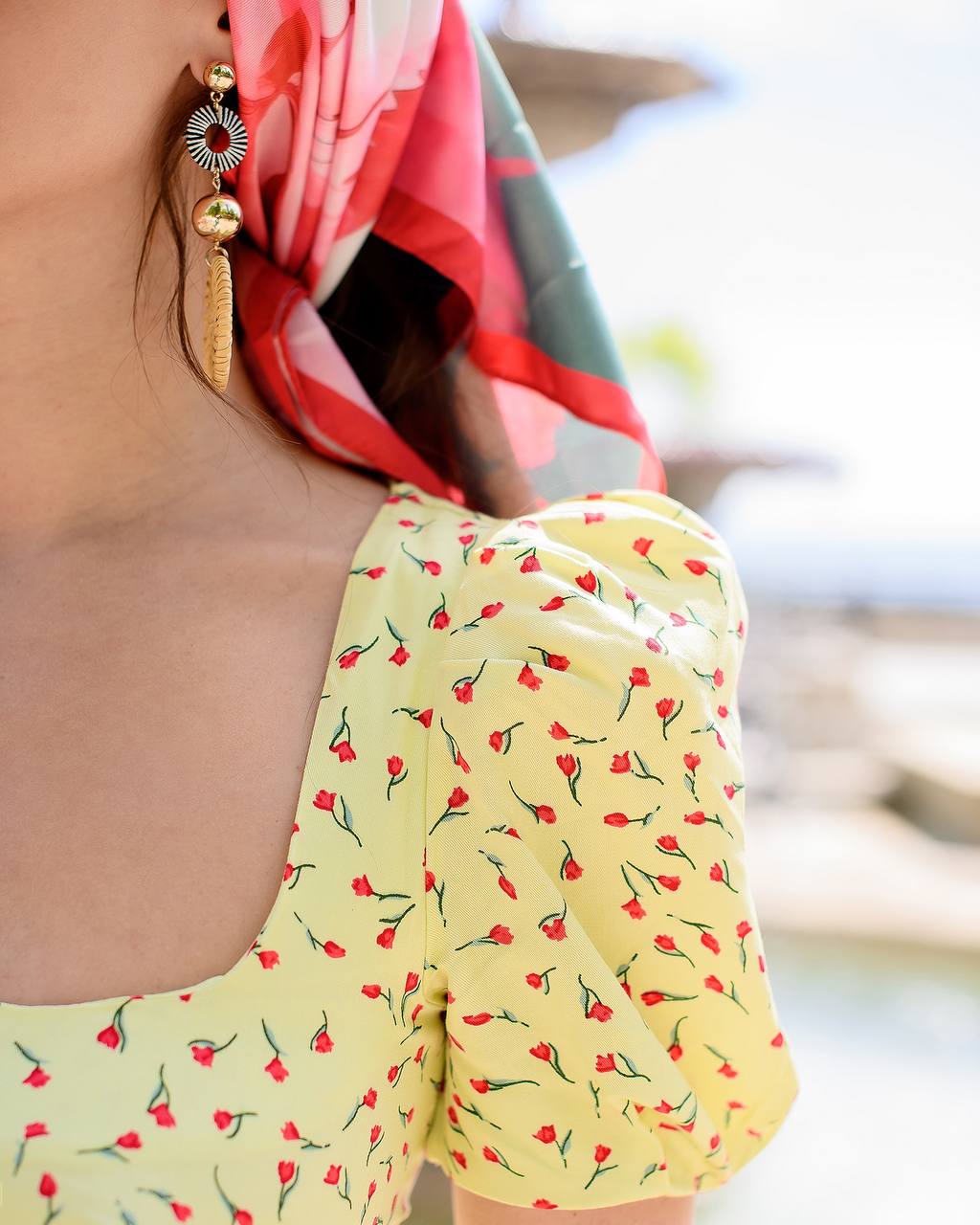 Yellow top with red floral pattern worn by a person with a blurred background
