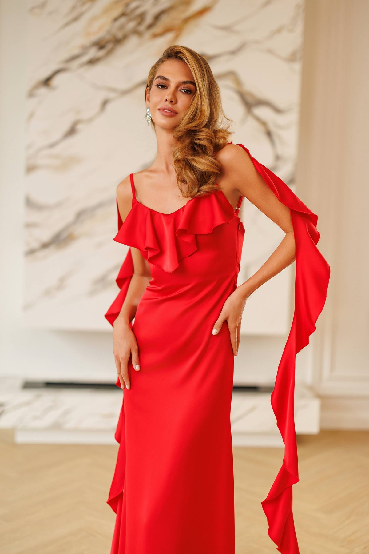 Woman wearing a red evening gown with ruffled details in an elegant indoor setting.
