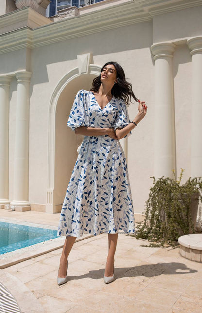 Woman in a floral dress standing by a pool with classical architecture in the background