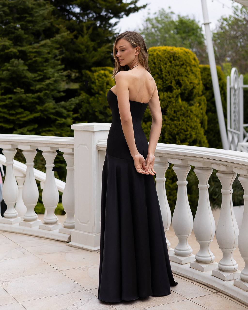 Woman in a black strapless gown standing on a balcony with greenery in the background