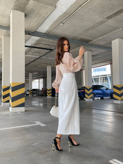 Woman in a parking garage wearing a light pink blouse and white pants.