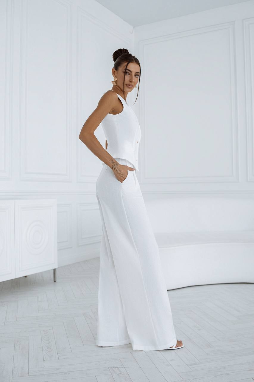 Woman wearing a white sleeveless top and wide-leg pants in a minimalistic room.