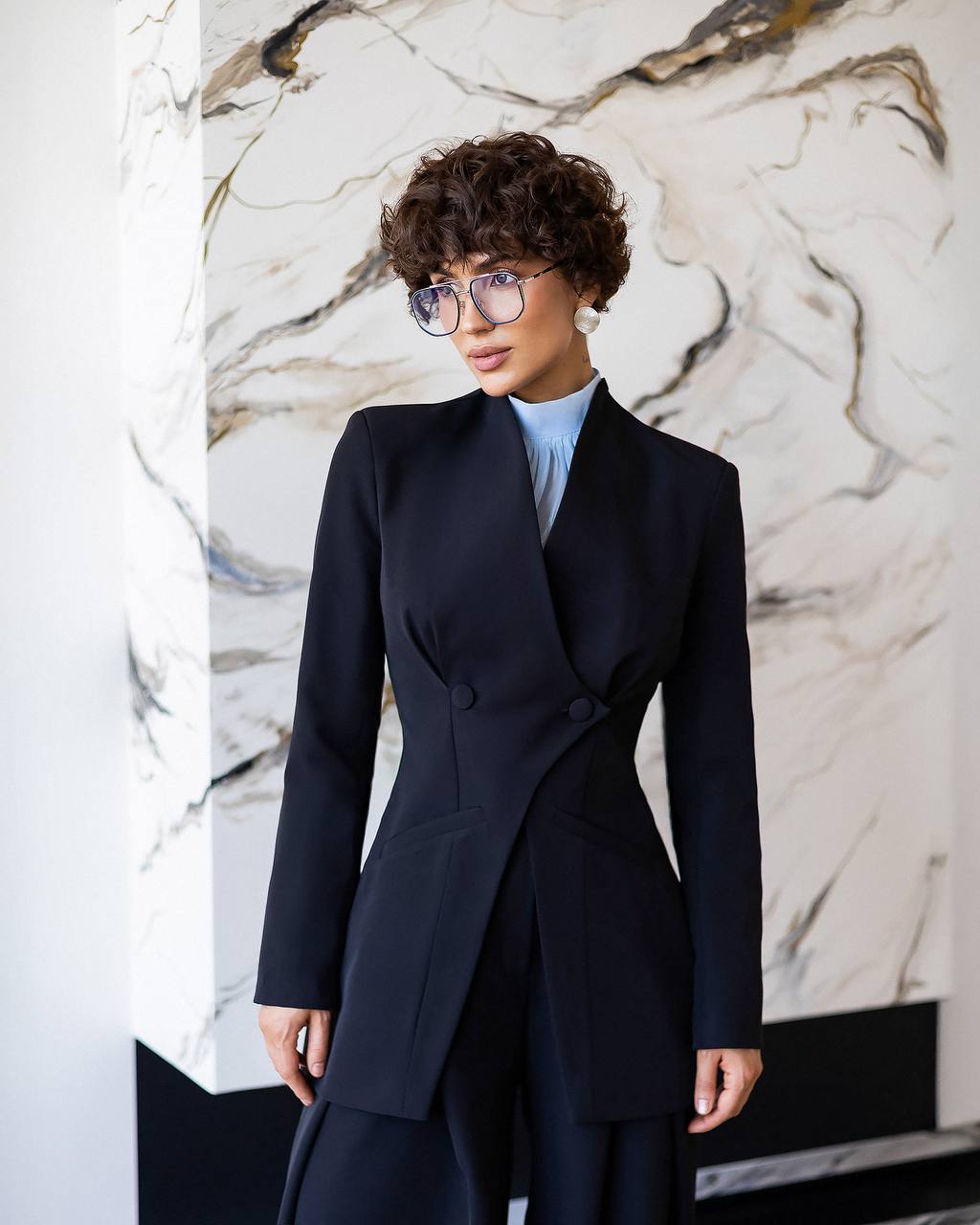 Woman wearing a dark blue coat against a marble wall