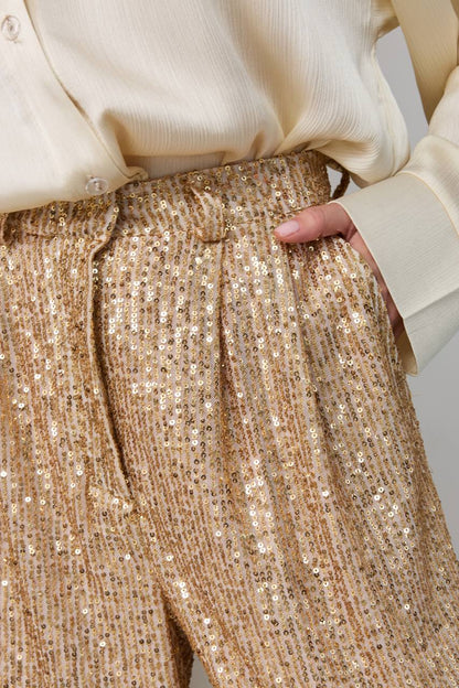 Close-up of gold sequin pants with a beige blouse.