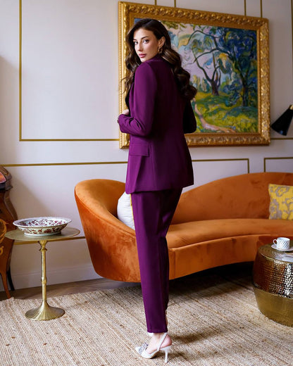 Woman in a purple suit standing in a stylish room with an orange sofa and framed artwork.