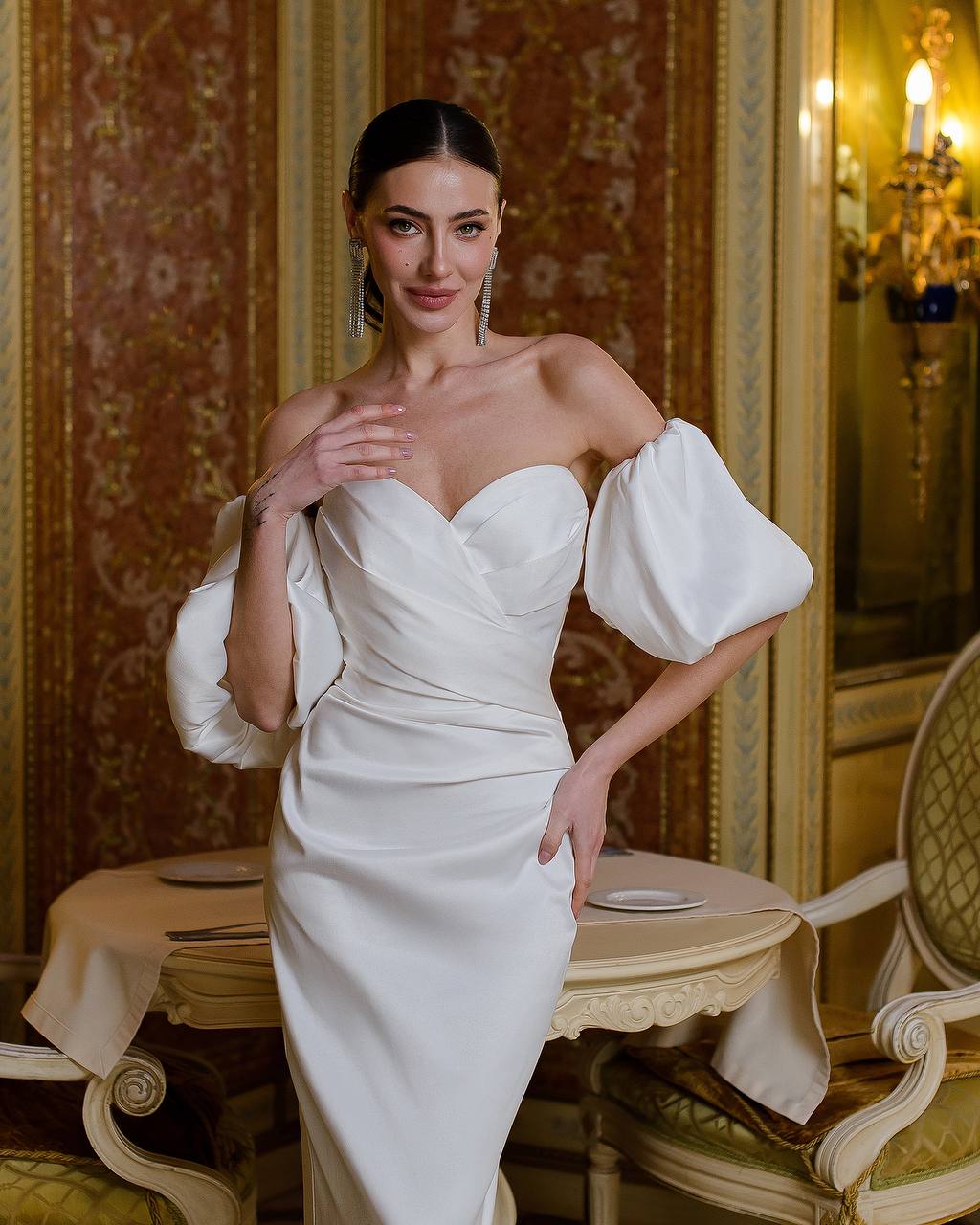 Woman in a white dress with puffed sleeves standing in an elegant room.