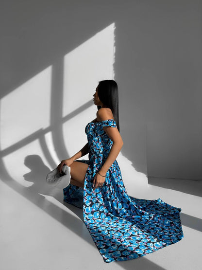 Woman in a blue floral dress standing against a white wall with a shadow.