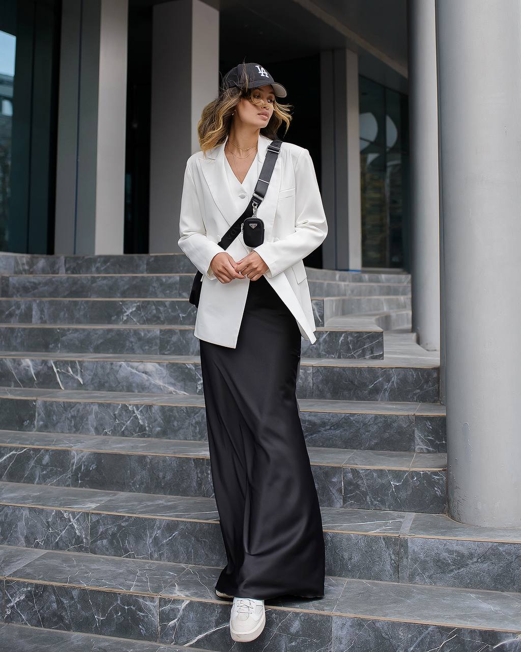Woman in a white blazer and black pants standing on marble steps.