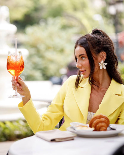 Woman in a yellow blazer holding a glass of orange cocktail outdoors