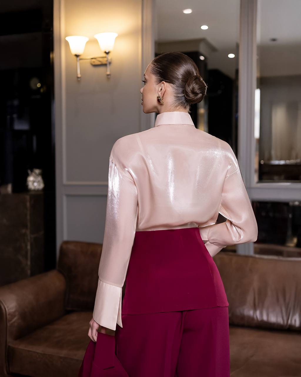 Person wearing a light pink blouse and maroon pants in an indoor setting.