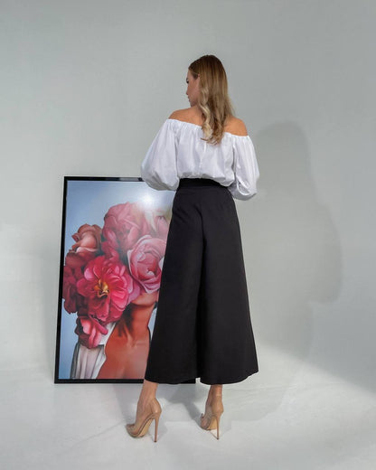 Woman in a white blouse and black skirt standing in front of a floral painting.
