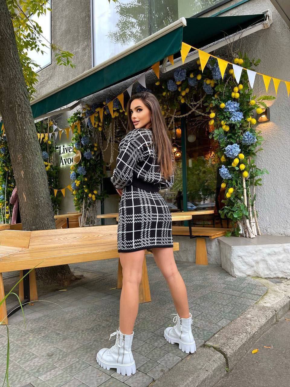 Woman in a black and white checkered outfit standing in front of a decorated outdoor cafe.